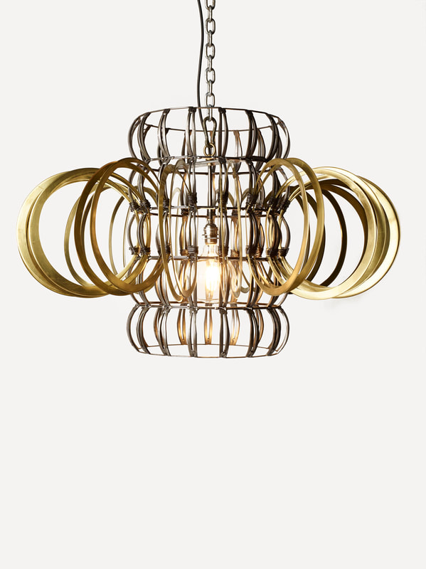 Suspended sculptural lighting created by Lucy Slivinski using scrap metal to form a vertical standing cylinder with brass rings encircling it perpendicularly. Single bulb inside.