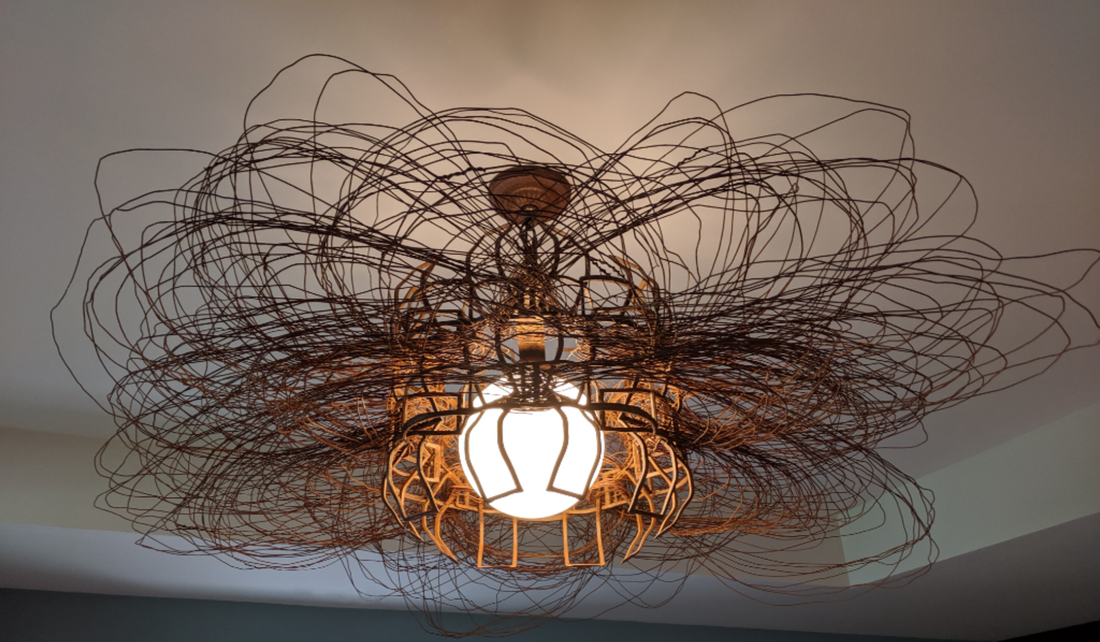 Artistic ceiling light made from rust colored salvaged metal and wire woven in numerous loops around the center form and glass globe. Created by Lucy Slivinski.