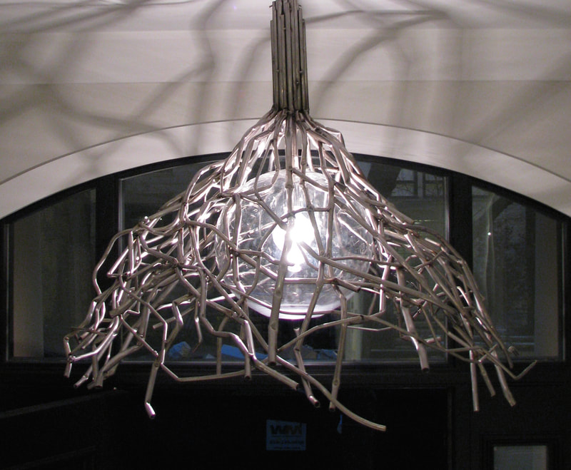 Artistic ceiling light made from stainlesss steel tubes conjoined at the top and spreading outwards to create a conical form surrounding a single glass globe. Created by Lucy Slivinski.  