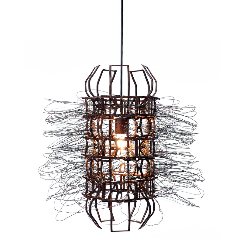 Small suspended artistic light with rust colored metal frame around single bulb and wire looping outward. Created by Lucy Slivinski.
