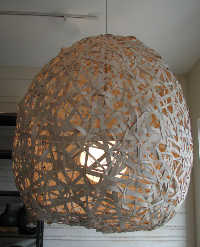 Large suspended woven light made from wooden reed and wire hand woven into a spherical shape encasing a single glass globe while open at the bottom. Created by Lucy Slivinski.