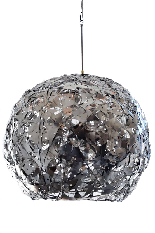 Suspended artistic light made from salvaged stainless steel wire hand woven into a spherical shape encasing a single glass globe while open at the bottom. Created by Lucy Slivinski.