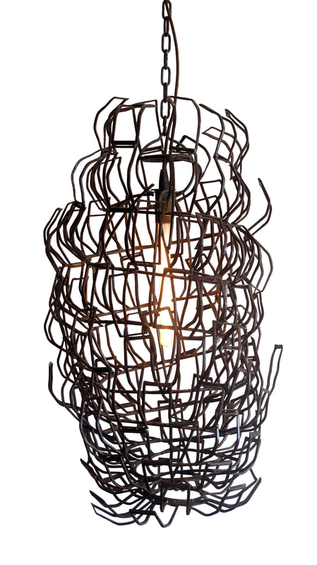 Suspended artistic lighting made from pieces of rust colored scrap metal welded to form a bulbous shape encasing a single long bulb inside. Created by Lucy Slivinski.