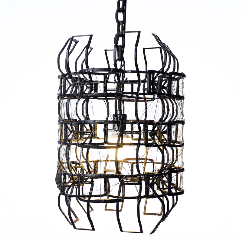Small suspended artistic light with black colored metal frame around single bulb and wire tightly woven in. Created by Lucy Slivinski.
