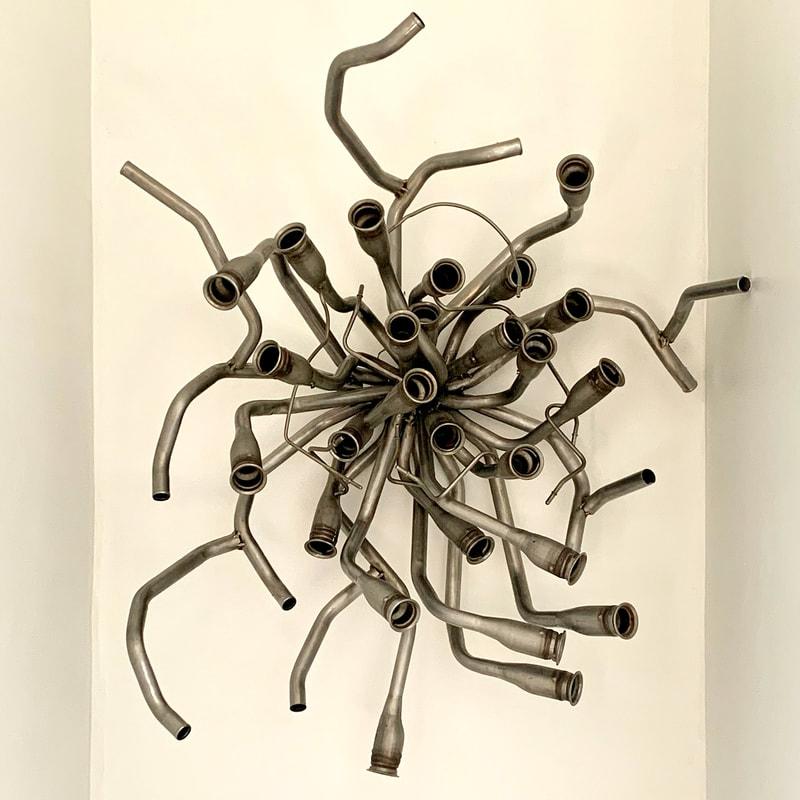 Wall mounted abstract metal sculpture made with salvaged metal tubes welded together at a central point and protruding outward. Created by Lucy Slivinski.
