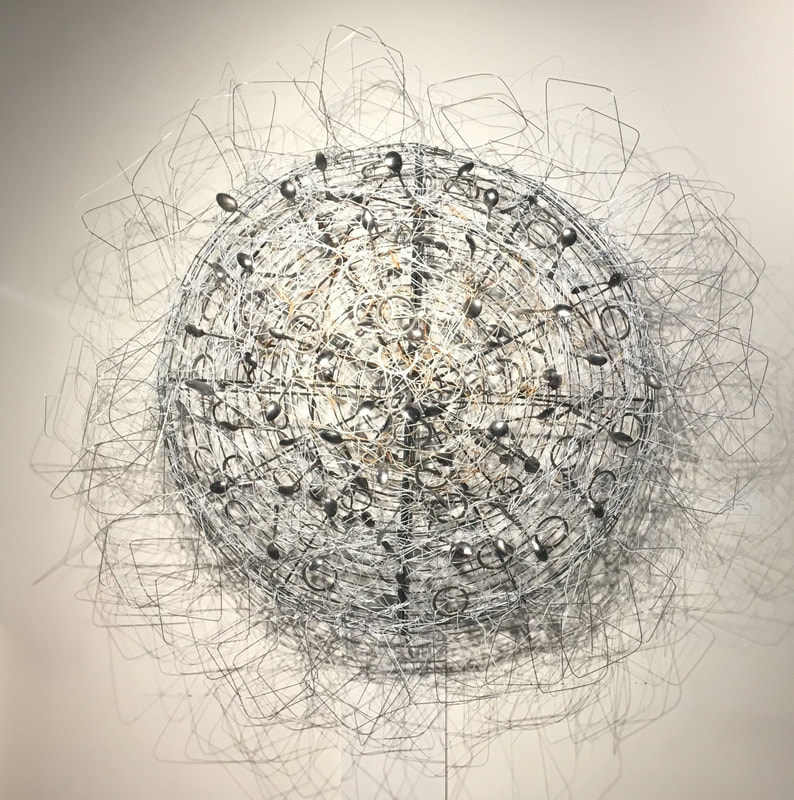Large wall mounted abstract sculpture made from found objects.  Large metal fan grate with spoons and white coat hangers woven in. Created by Lucy Slivinski. 