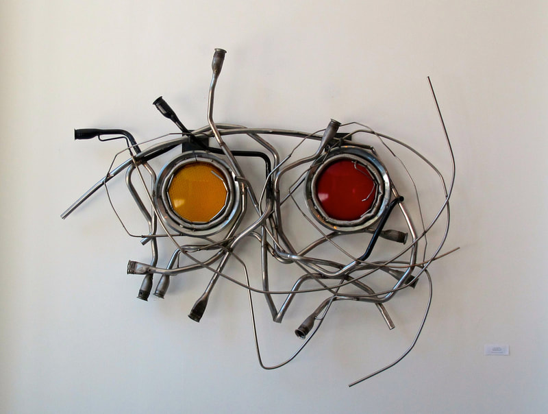 Wall mounted abstract metal sculpture made from salvage metal and two traffic light lenses. Created by Lucy Slivinski. 