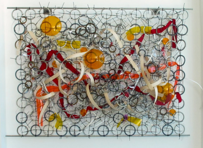 Large wall mounted abstract sculpture made from found objects.  Metal rings zip tied together into a sheet with colored plastic wooden reed and traffic light lenses  woven in. Created by Lucy Slivinski. 